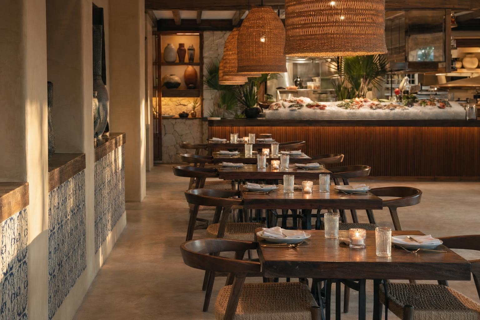 Mar de Oro dining room — long dark wood tables, woven pendants in a row, blue-and-white Mexican tile, raw bar at the back